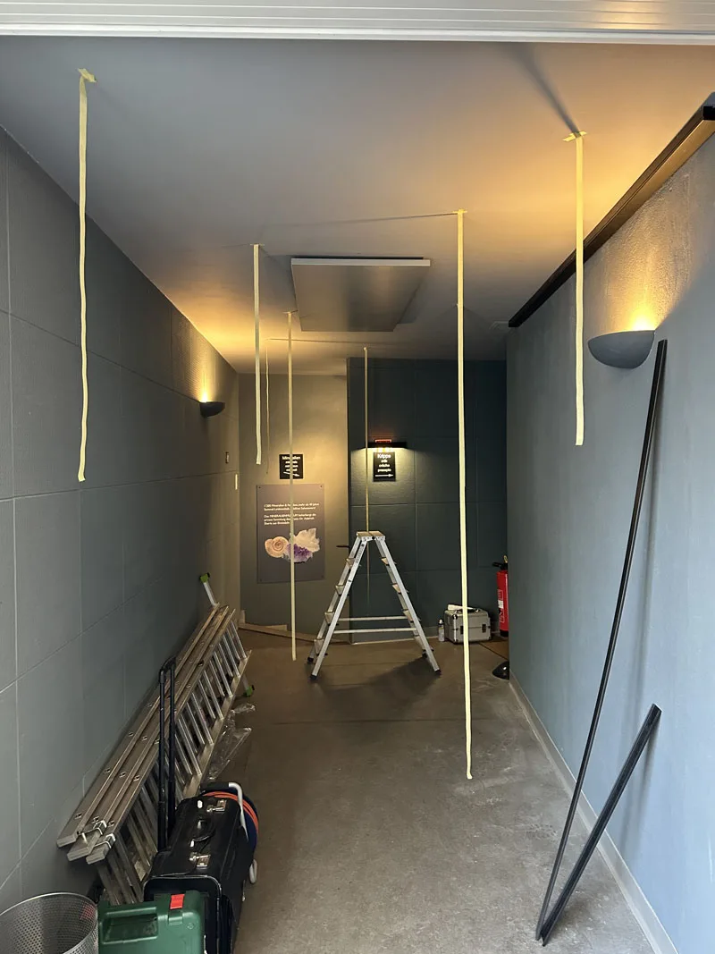 Unlit light ropes hanging in the gallery during the install, a step ladder standing under the ceiling mounts