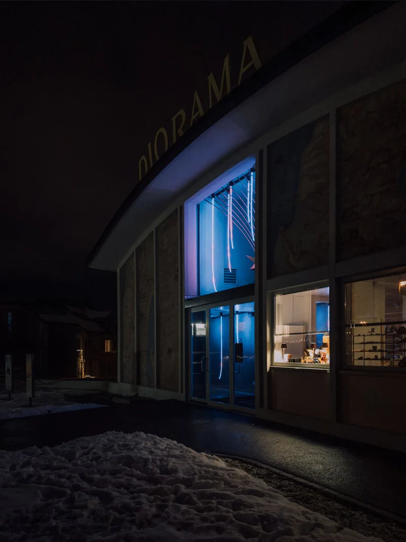 The museum's glass frontage glowing blue at night, snow banked outside and the gold DIORAMA sign above