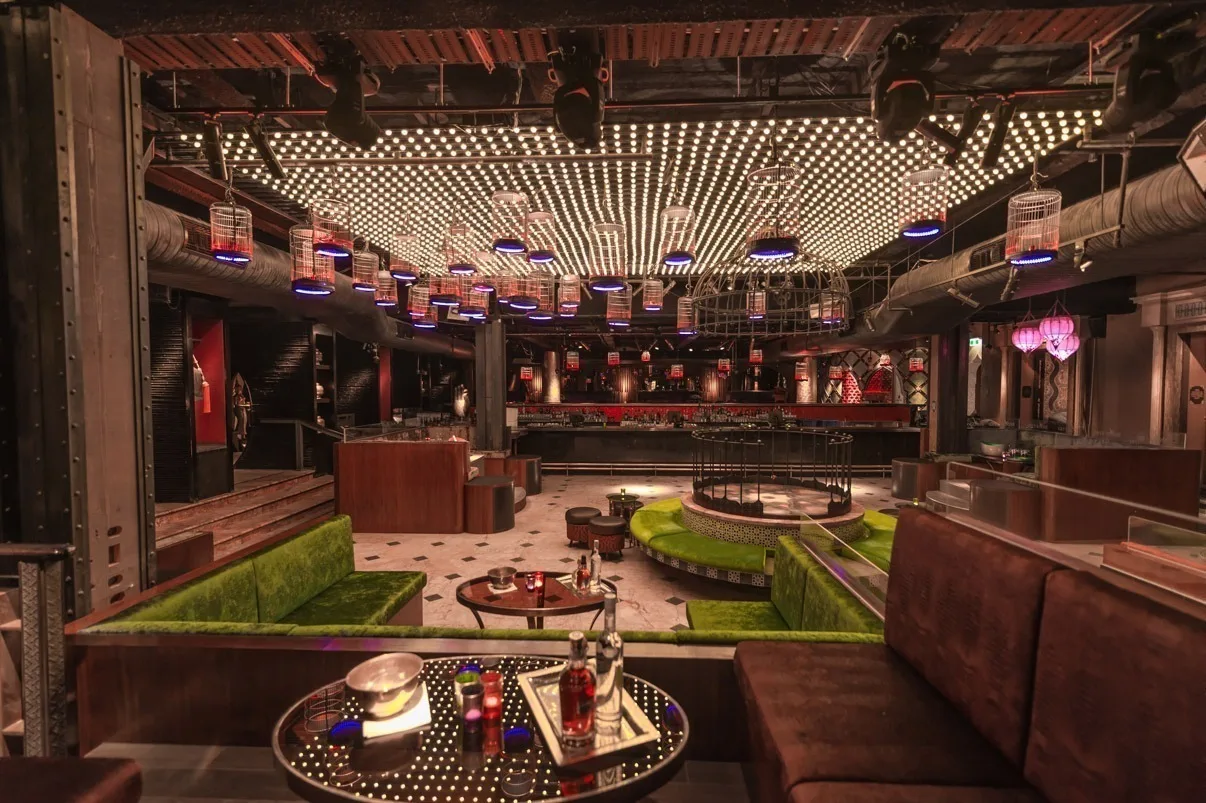 The room from the upper level, ceiling dots in warm white above a green carpeted lounge and a brass tray table in the foreground