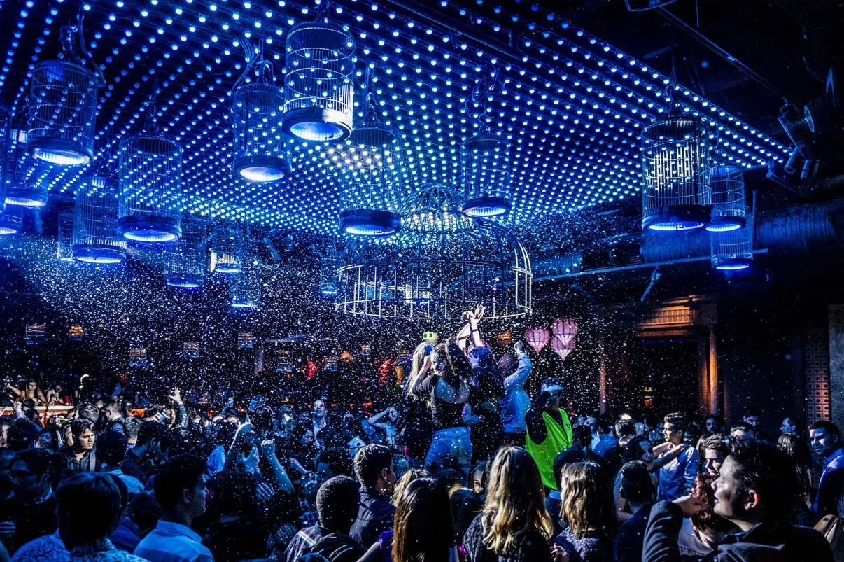 From within the crowd looking towards the stage, blue and white ceiling dots overhead and confetti in the air