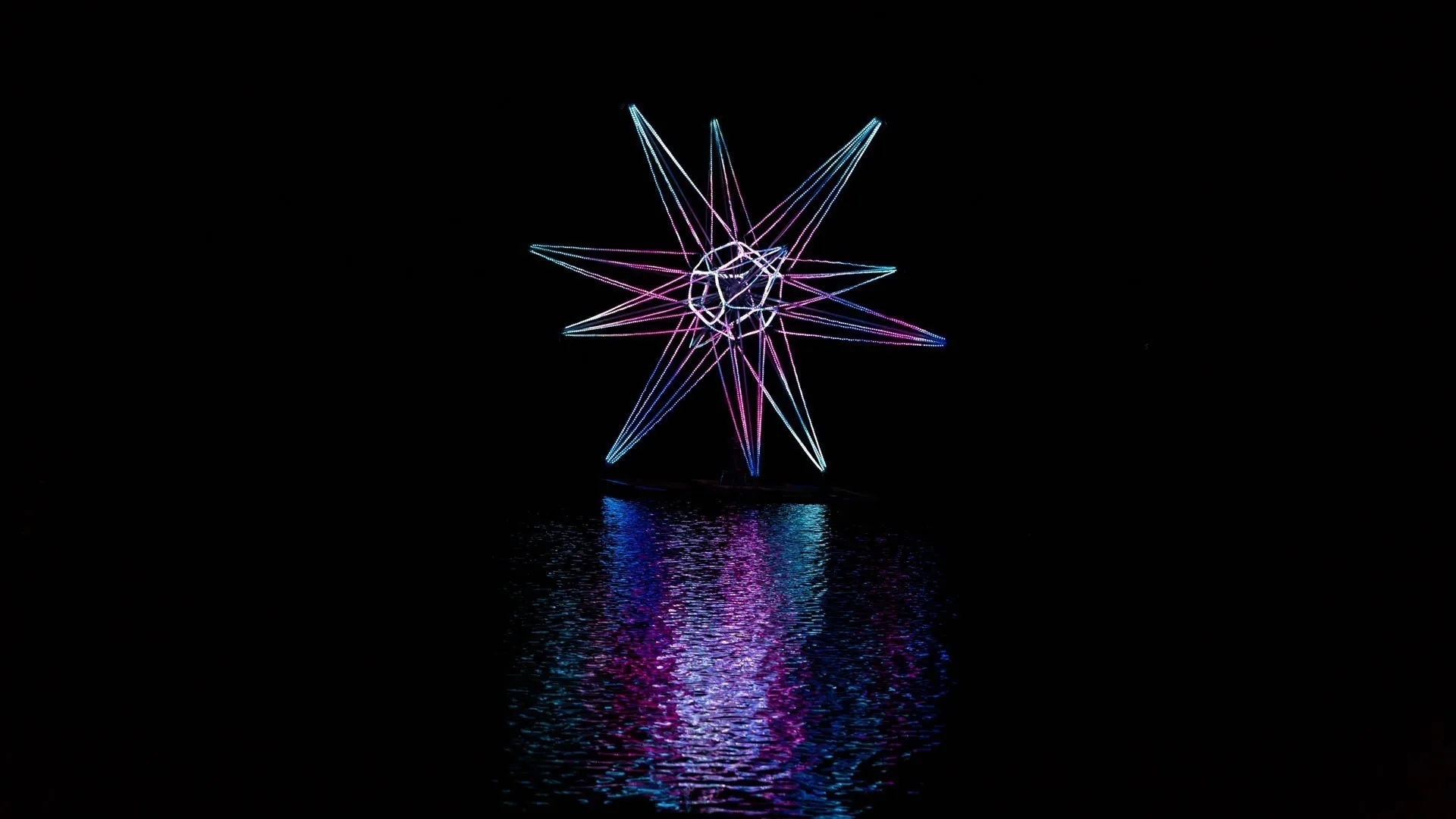 The star seen smaller against the black water, violet and blue spokes with a broad rippled reflection beneath it