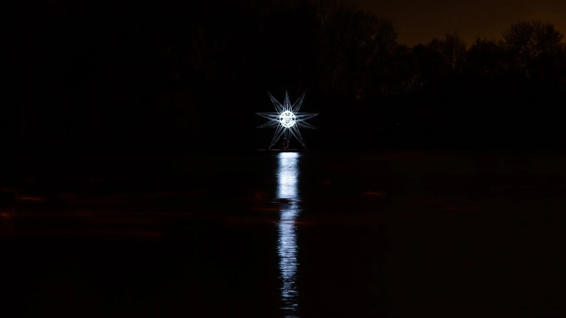 From the far side of the lake, the sculpture reduced to a single white point with a long reflection down the water and trees on the skyline