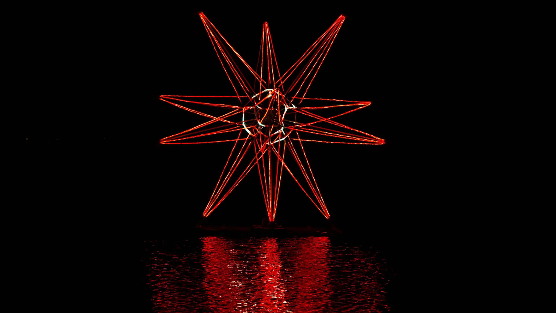The whole star running deep red, the steel wire core picked out white at the centre and red light spilling across the lake