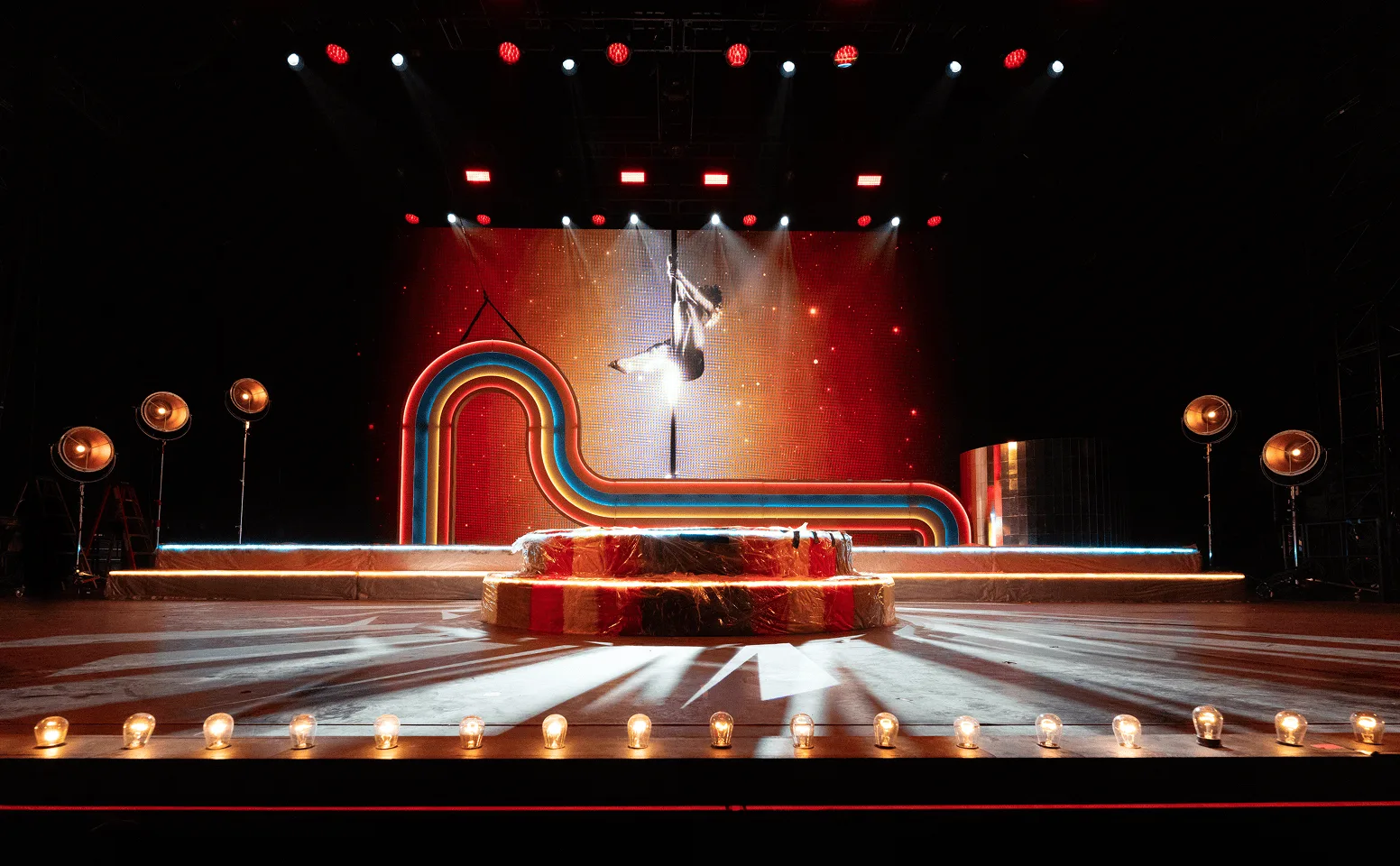 The bare stage in warm red, the rainbow arch and fur steps waiting with an aerialist hanging above the thrust
