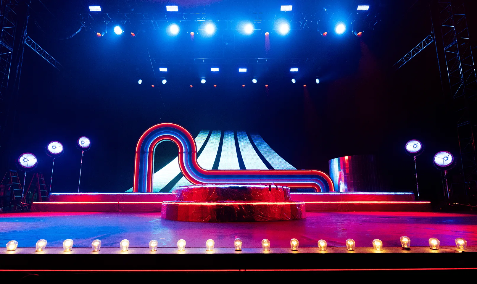 Cool blue wash over the empty set, overhead fixtures picking out the arch and the ring of footlights along the stage lip