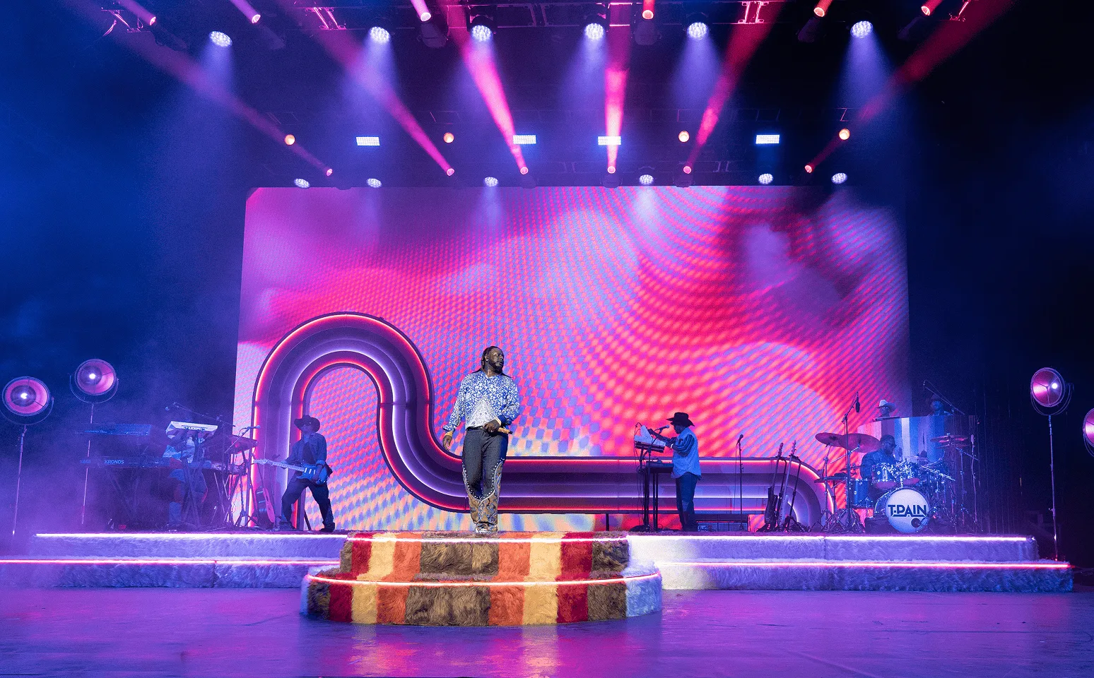 Wide view of the stage in magenta and violet, the arch traced in colour above the striped fur riser