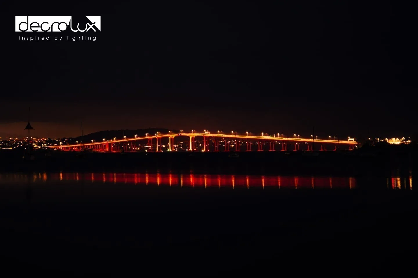 The bridge picked out in warm orange along its full length, seen across black water with broken reflections