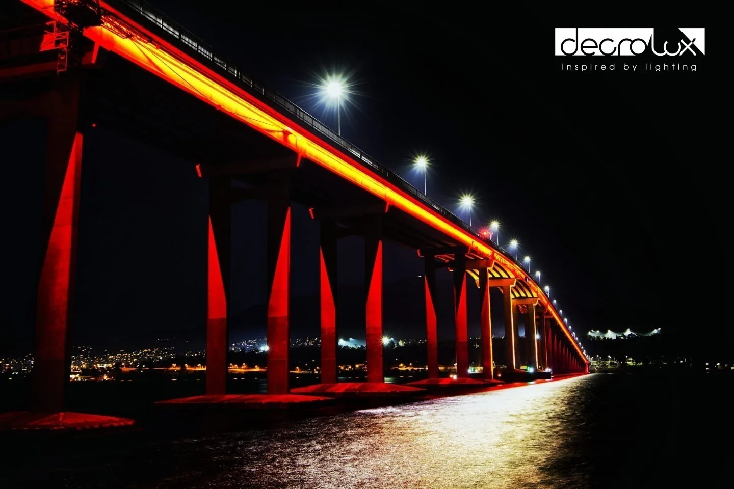Looking along the line of red piers from beneath, a broad gold pool of light on the water below the span