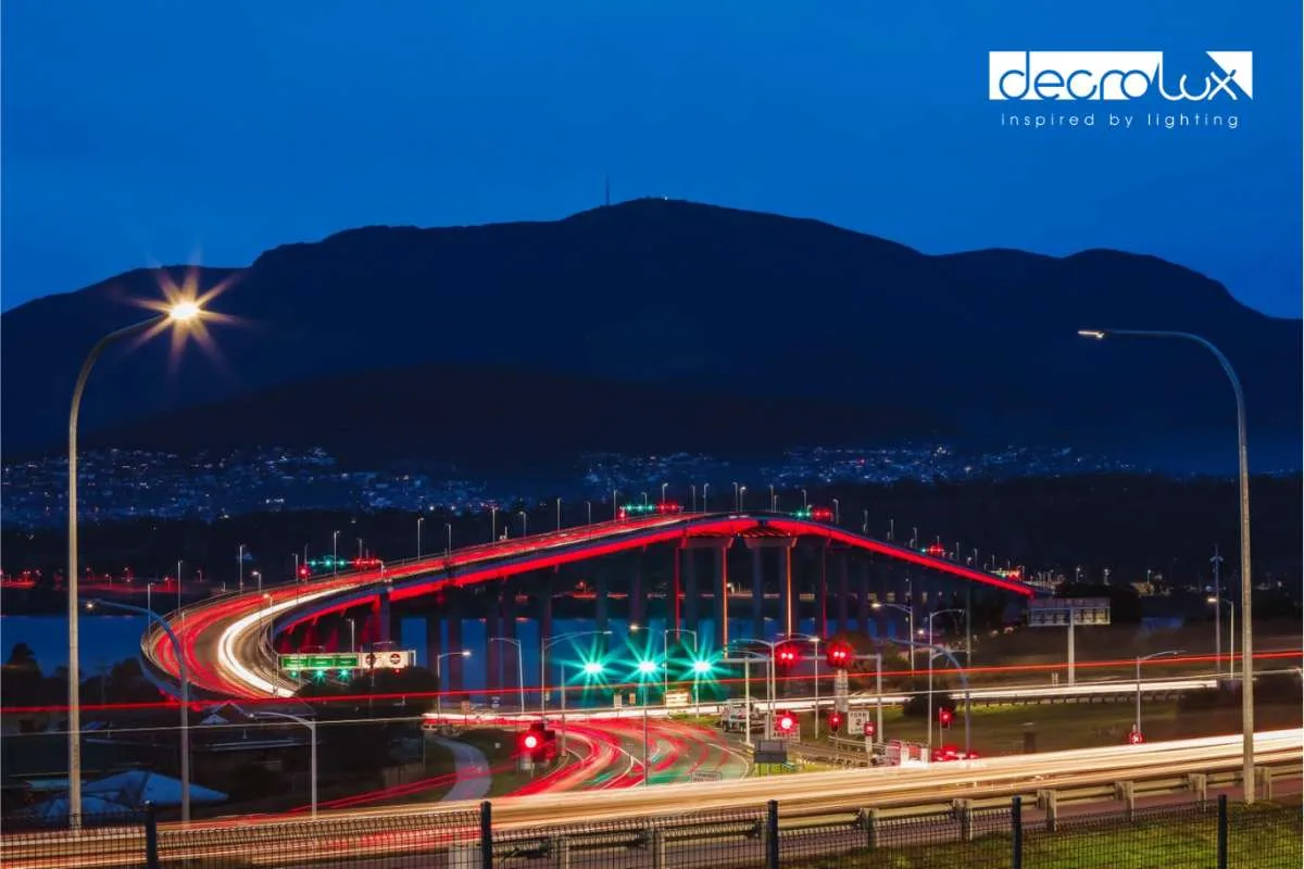 Blue hour view from the road approach, red vehicle trails looping onto the bridge with the mountain rising behind
