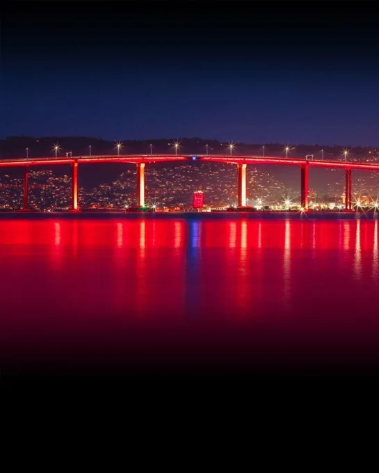 The full span glowing red across calm water at night, the reflection running the width of the river toward the city