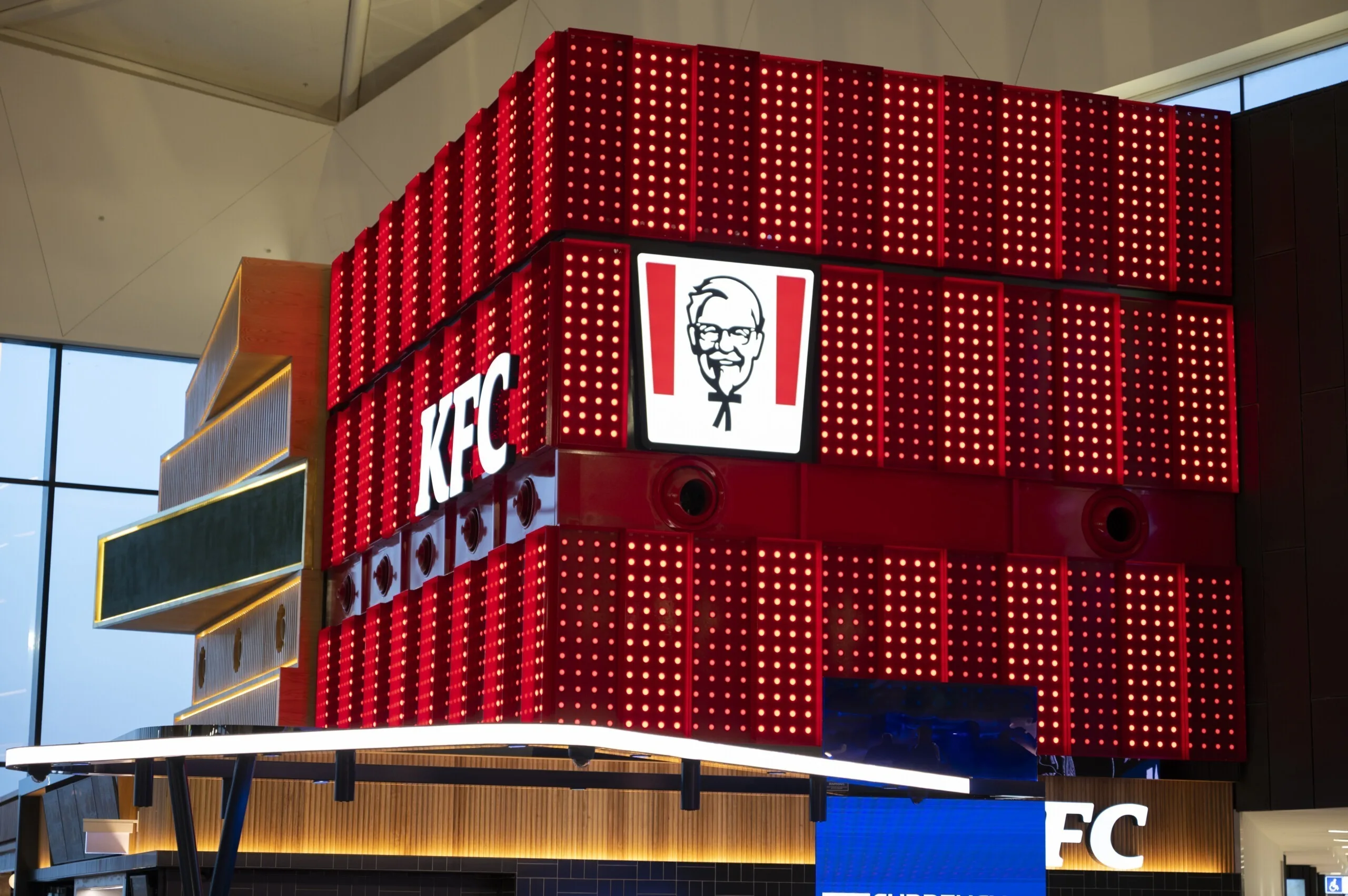 Corner of the lit box from below, the logo panel facing the white canopy over the counter with a currency exchange sign to the right