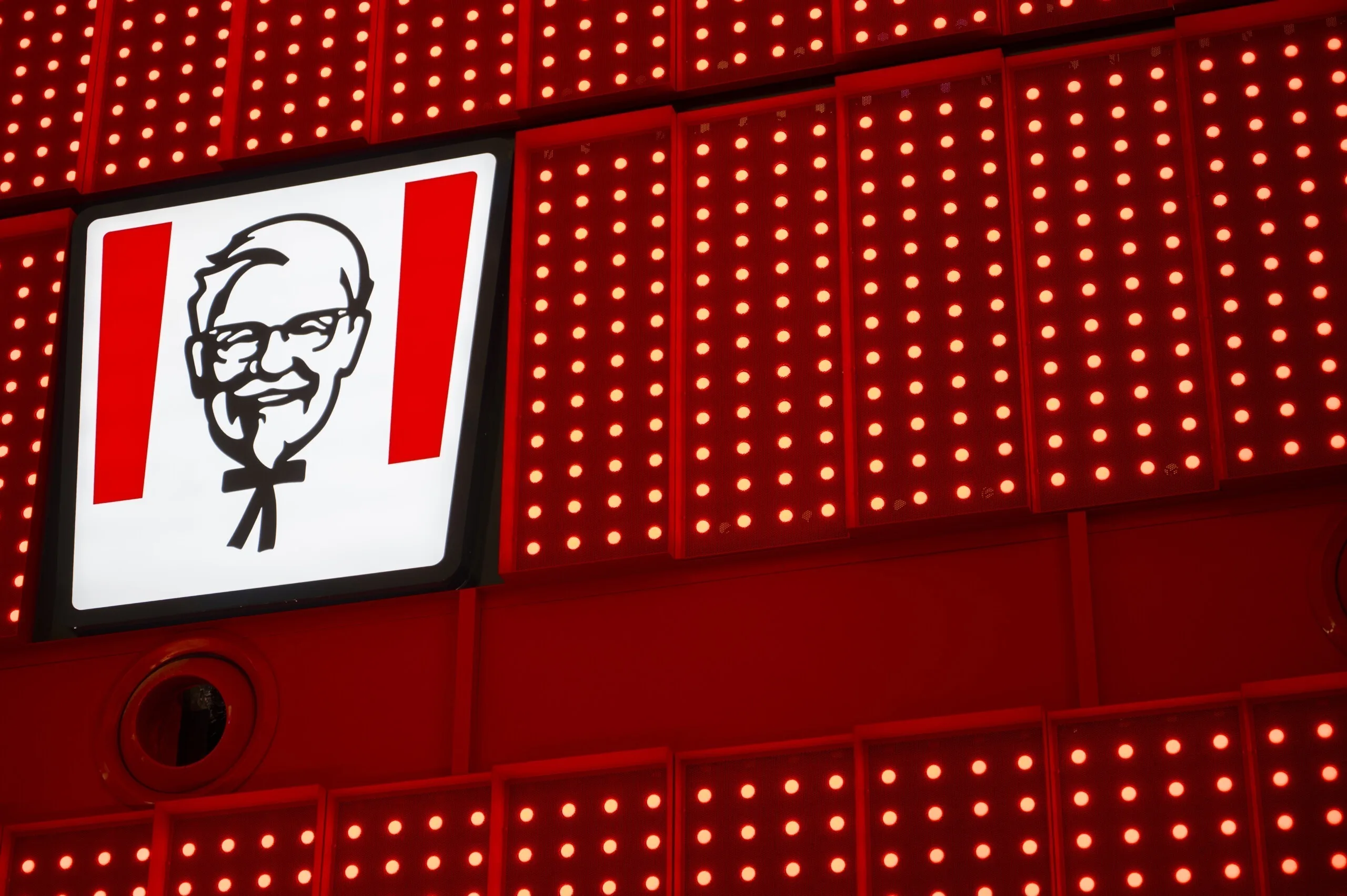 Straight-on close-up of the Colonel Sanders logo panel, red pixel-dot panels filling the frame around it