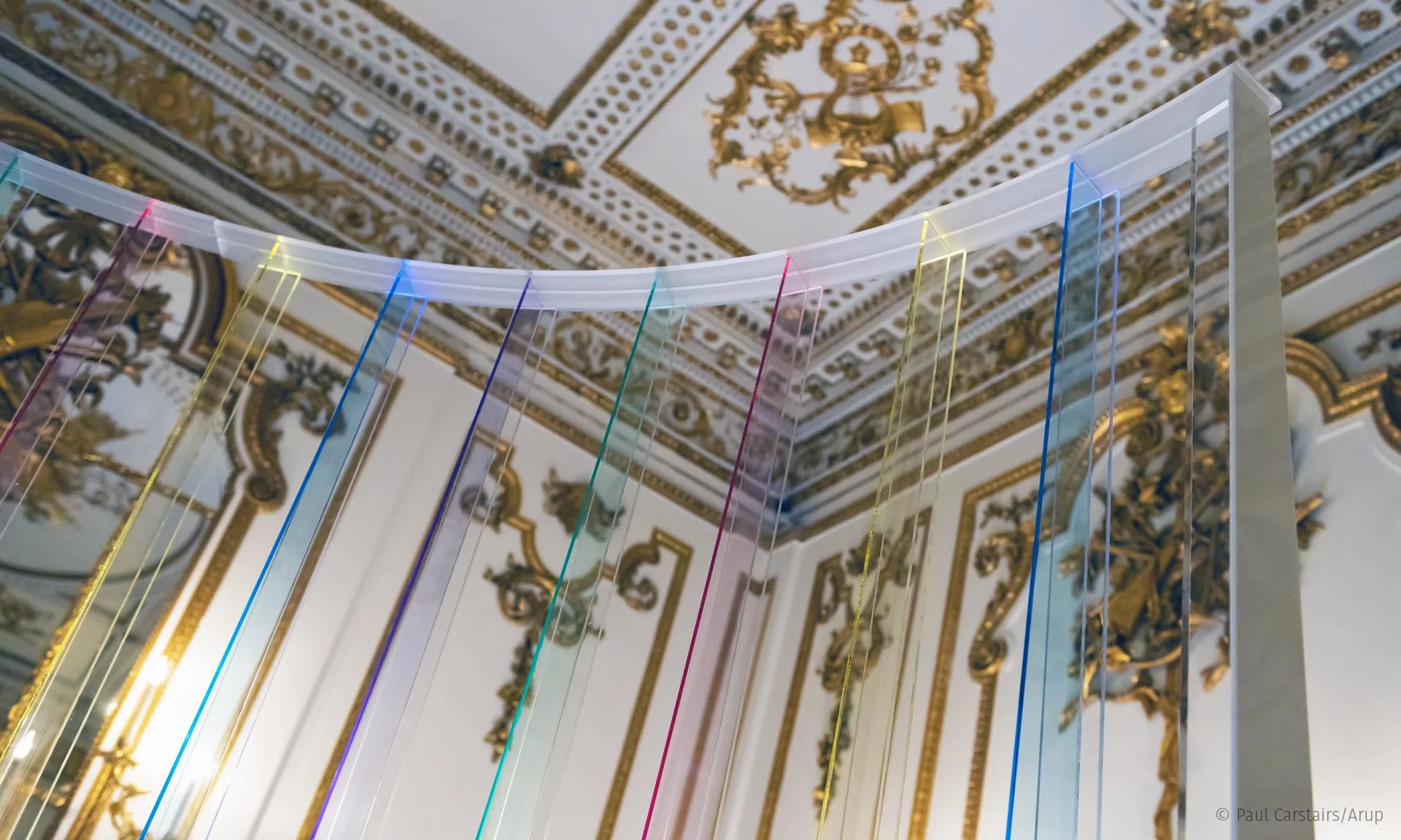 Looking up through the acrylic slats to the white and gold plasterwork ceiling, coloured lines catching in the edges