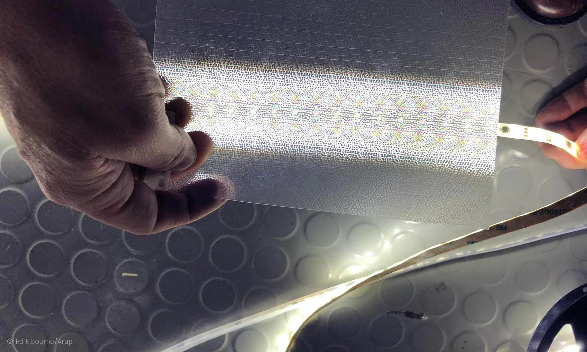 Hands trimming a length of warm white LED tape on a workbench, scissors and the cut end alongside