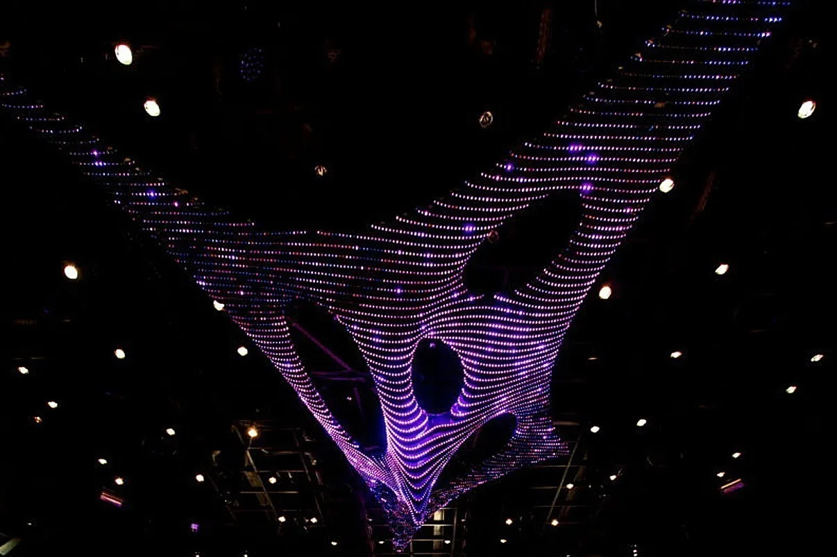 Looking straight up at the underside of the sculpture in violet, recessed ceiling downlights scattered around it