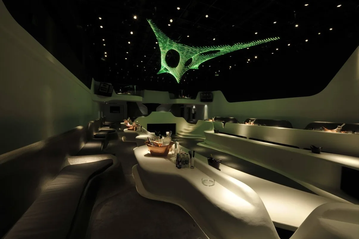 The sculpture in green over an empty lounge, white curved banquettes and set tables in the foreground