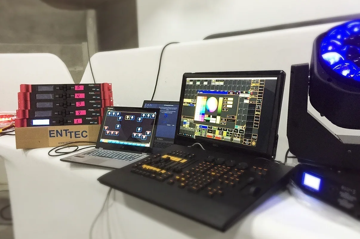 Commissioning bench on a white table, two laptops, a lighting console and an ENTTEC carton beside a blue moving head