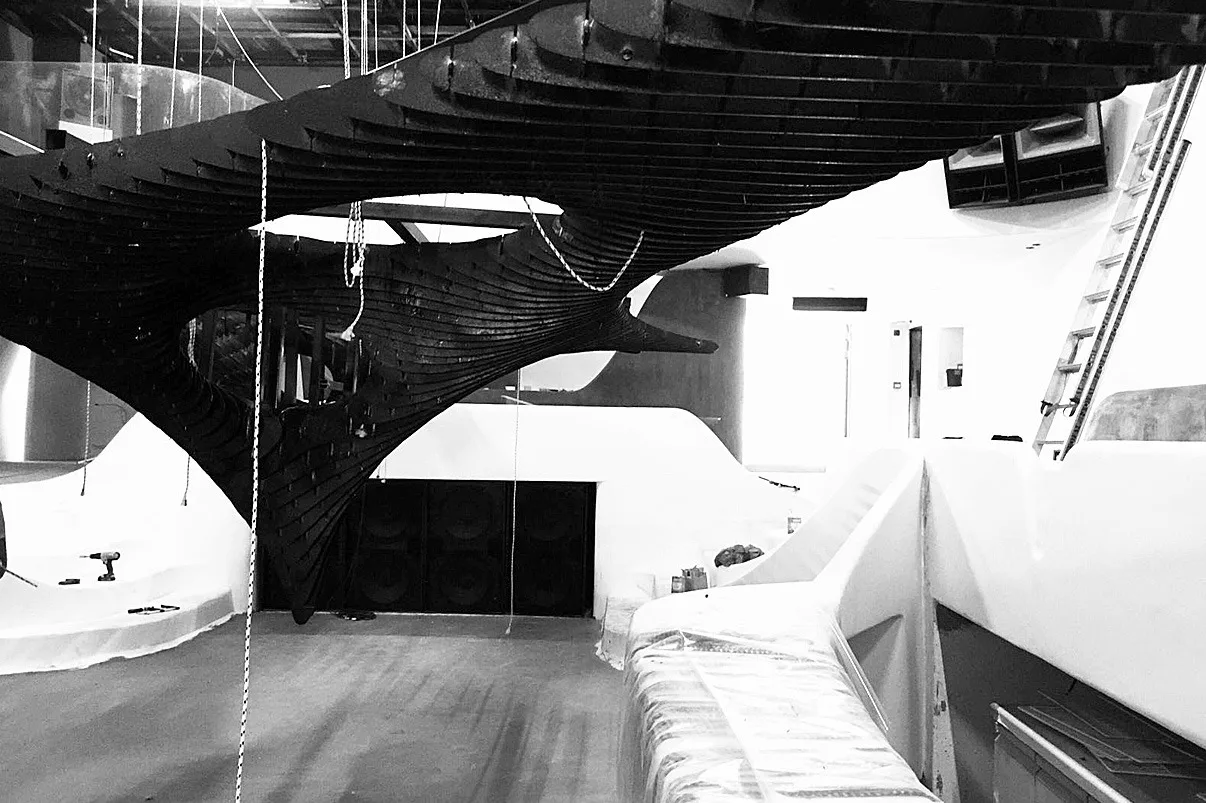 Black and white view of the bare sculpture skeleton hung over the unfinished venue during the fit out
