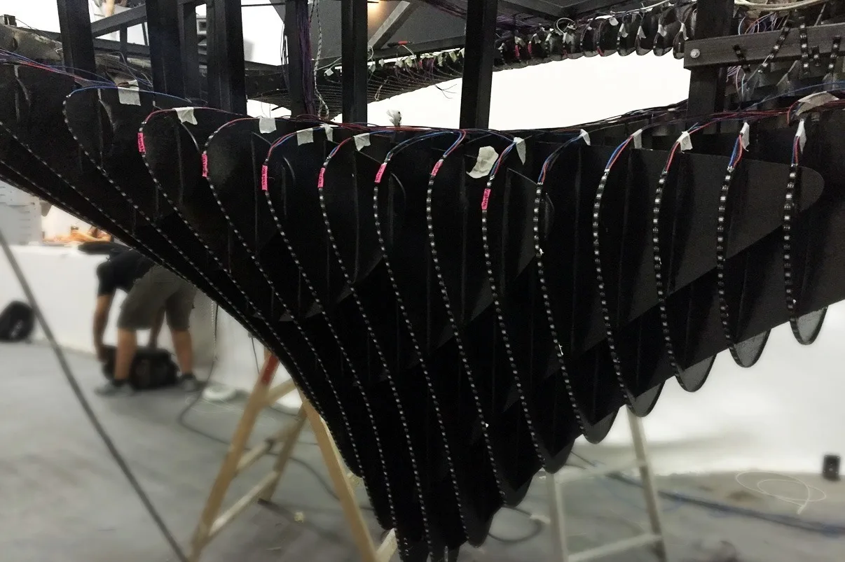 Underside of the sculpture mid build, black fins hanging in a curve with an installer working below