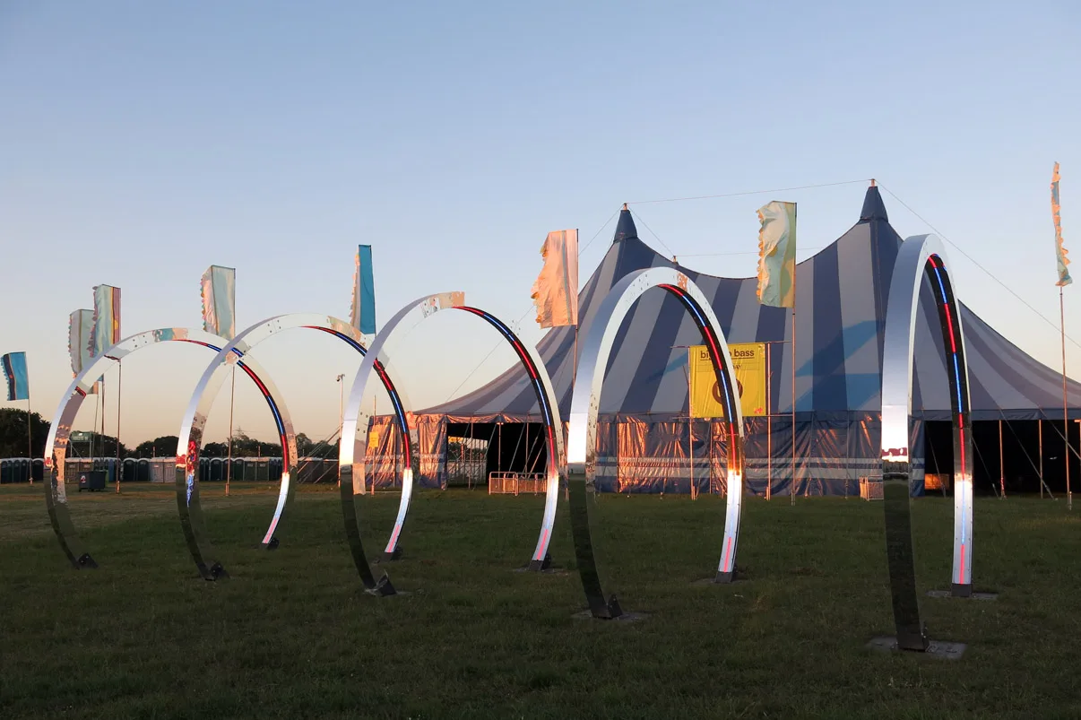 The full row of hoops standing on grass at dusk, a striped big top and festival flags behind them
