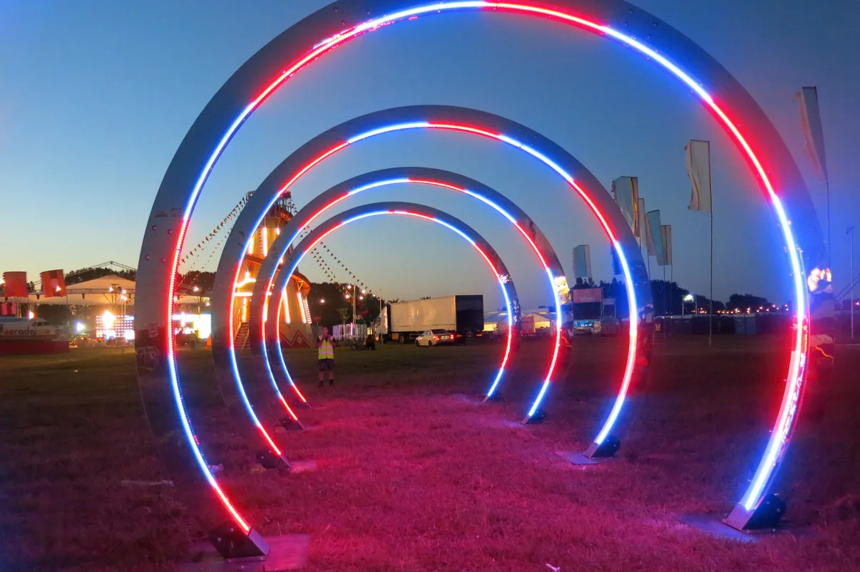 The tunnel of hoops lit red, white and blue after dark, magenta light spilling onto the grass