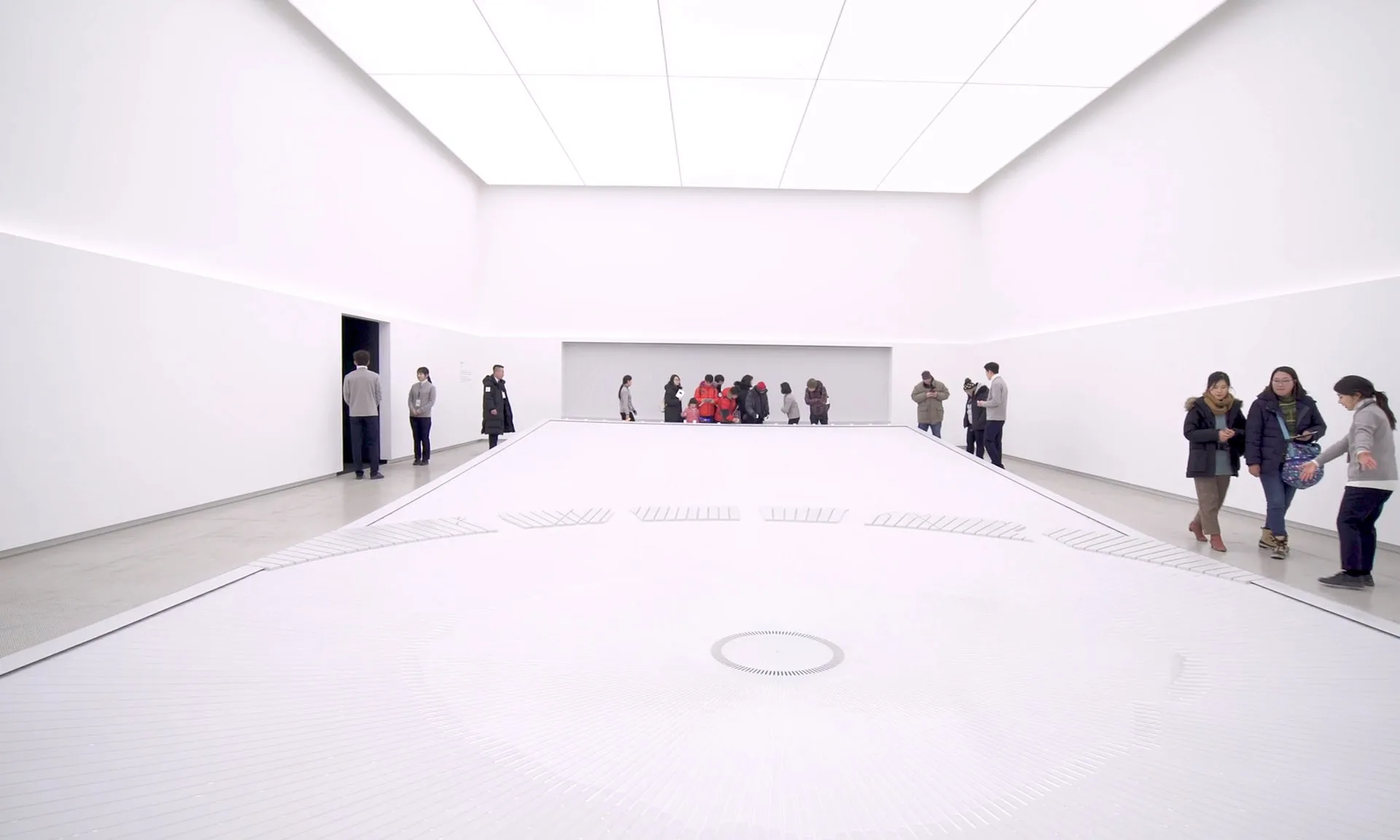 The stark white interior room, a shallow sheet of water across the floor and visitors gathered along the far wall