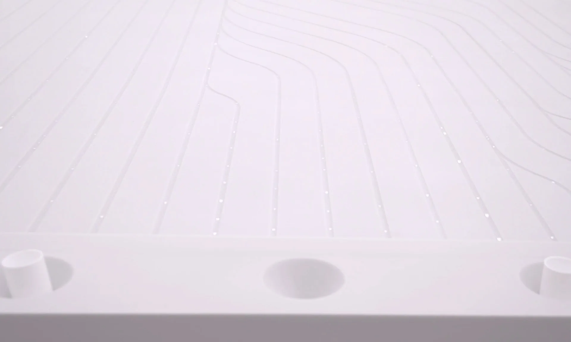 Close on the white hydrophobic surface, fine channels running away between rows of nozzle openings with droplets sitting on them