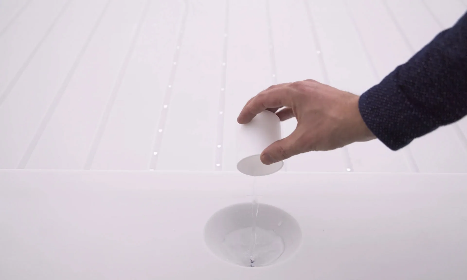 A visitor lowering a white cup over one of the nozzle openings, the surrounding channels beaded with water