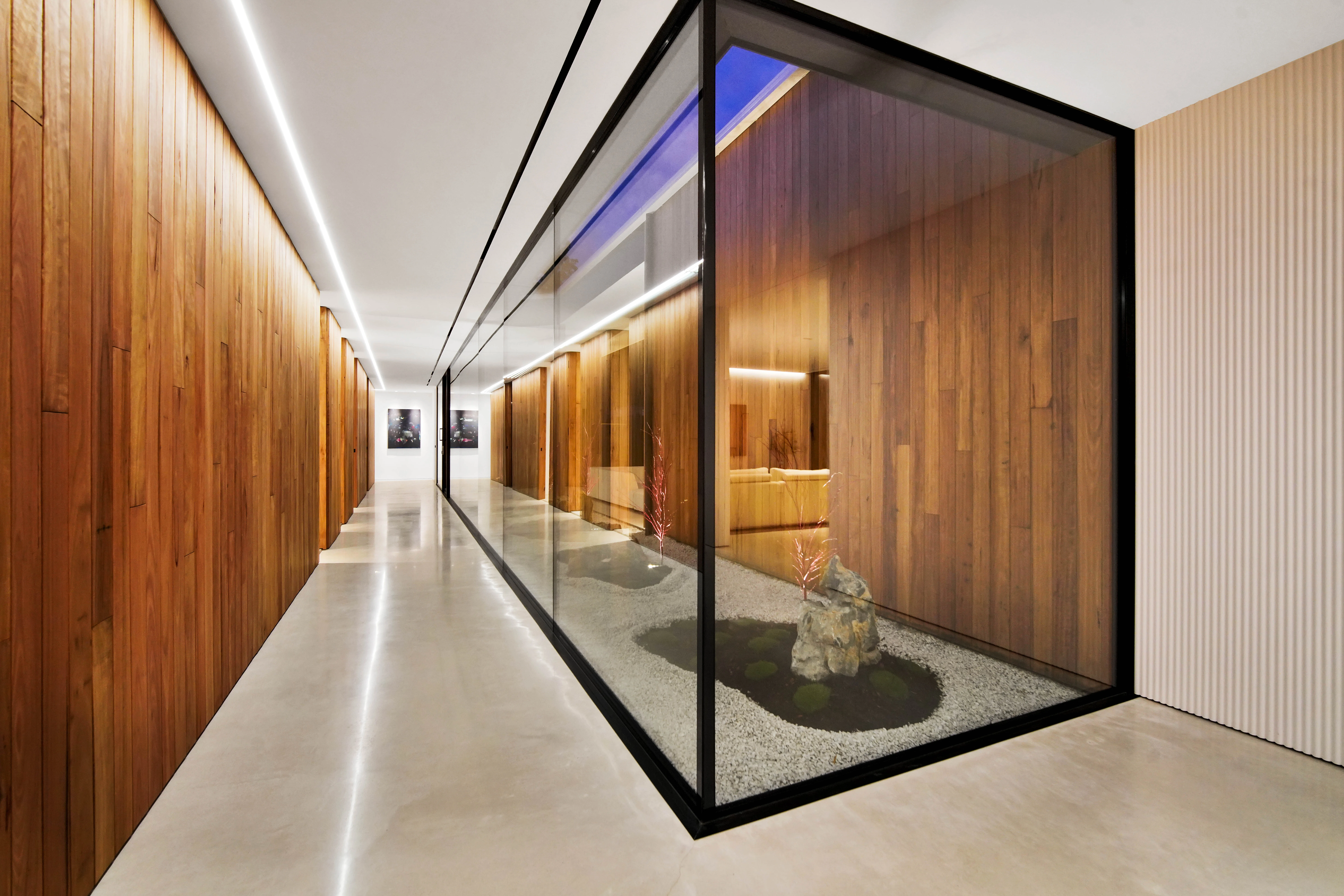Wider view along the hallway showing the full glazed courtyard box, the ceiling strip washing the timber wall